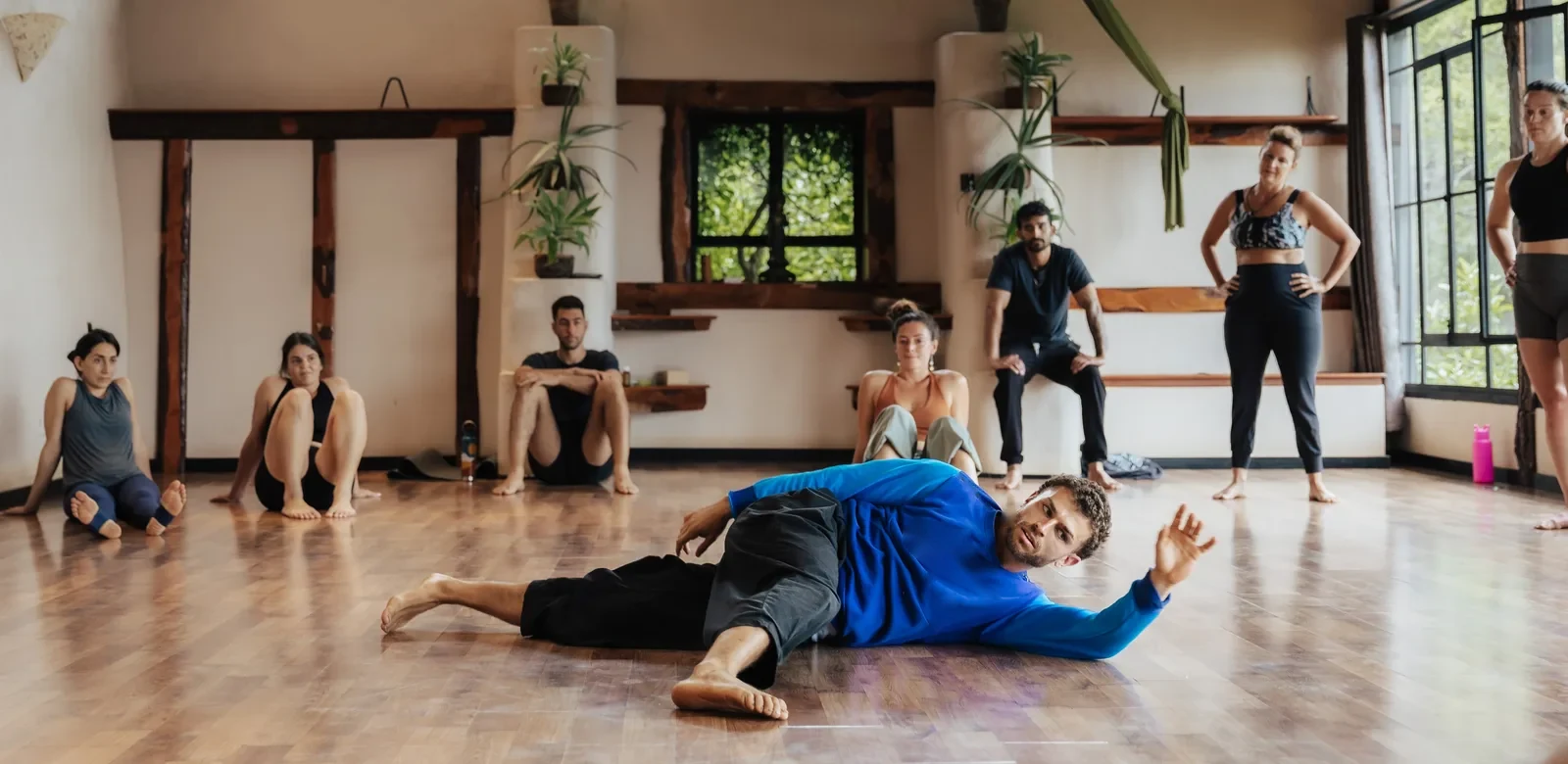 Omar demonstrating a floor movement while a group of workshop participants sit and stand around the studio watching